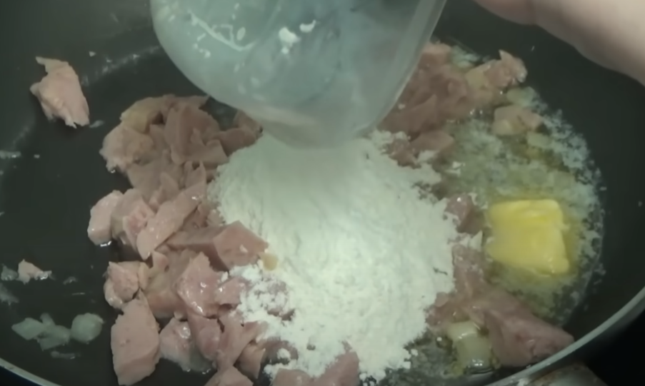 flour being poured on nondescript meat with butter melting beside in a pan